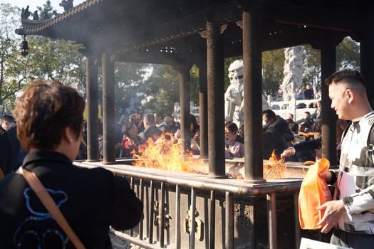 Beberapa orang membakar uang kertas sembahyang dan replika barang-barang di depan makam saat perayaan Qingming, sebuah tradisi kuno yang masih lestari hingga kini sebagai wujud penghormatan kepada leluhur. Aroma dupa dan asap pembakaran ritual ini memenuhi udara, menciptakan suasana khidmat dan reflektif di pemakaman.