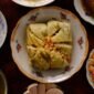 Meja makan dipenuhi aneka hidangan khas Peranakan yang memukau mata dengan warna-warni cerah dan aroma rempah menggoda, sebuah perayaan kekayaan kuliner yang melambangkan harmonisasi budaya. Setiap piring menceritakan warisan berharga dari generasi ke generasi, siap memanjakan lidah dan membawa kita pada perjalanan rasa yang tak terlupakan.