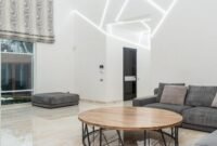 Ruang keluarga yang tertata rapi dengan banyak cahaya alami dan sentuhan tanaman hijau, mencerminkan prinsip-prinsip feng shui modern untuk menciptakan suasana yang harmonis dan menenangkan. Penataan ini bertujuan untuk memperlancar aliran energi positif di dalam rumah.