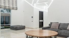 Ruang keluarga yang tertata rapi dengan banyak cahaya alami dan sentuhan tanaman hijau, mencerminkan prinsip-prinsip feng shui modern untuk menciptakan suasana yang harmonis dan menenangkan. Penataan ini bertujuan untuk memperlancar aliran energi positif di dalam rumah.