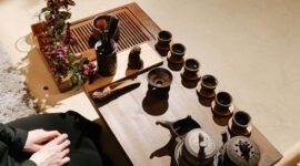 Sebuah poci teh yang sedang disajikan dengan cangkir-cangkir kecil di sekitarnya, merefleksikan kehangatan dan ritual sosial dalam tradisi minum teh yang berbeda-beda di seluruh dunia. Gambar ini menunjukkan keragaman cara menikmati teh, dari yang sederhana hingga upacara yang rumit, sebagai bagian tak terpisahkan dari kehidupan manusia.